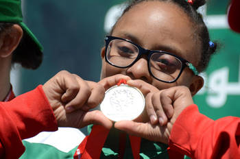 A little girl with glasses kisses her medal